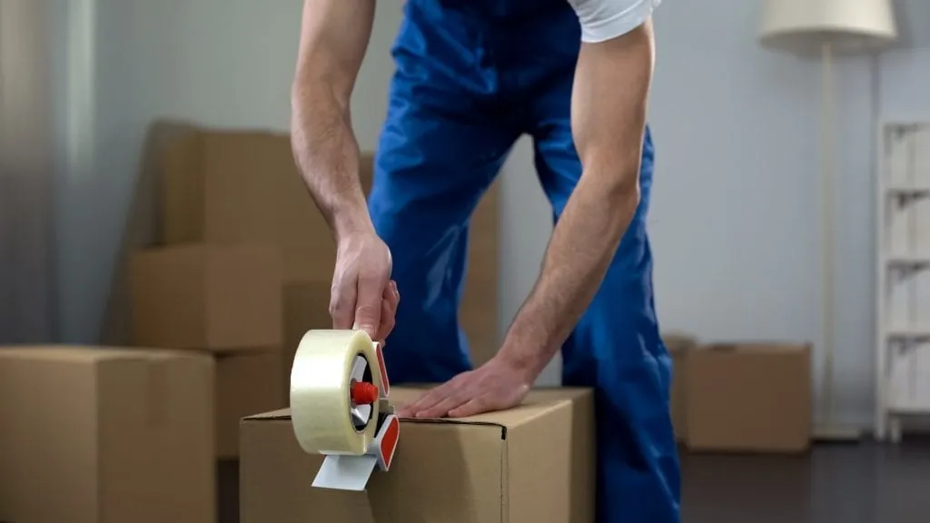 Mover taping a cardboard box in an apartment
