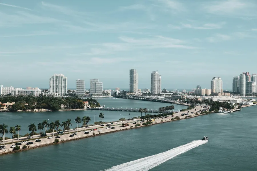 Aerial view of the MacArthur Causeway with traffic and palm trees, a speedboat wake in Biscayne Bay and Miami Beach condo towers behind