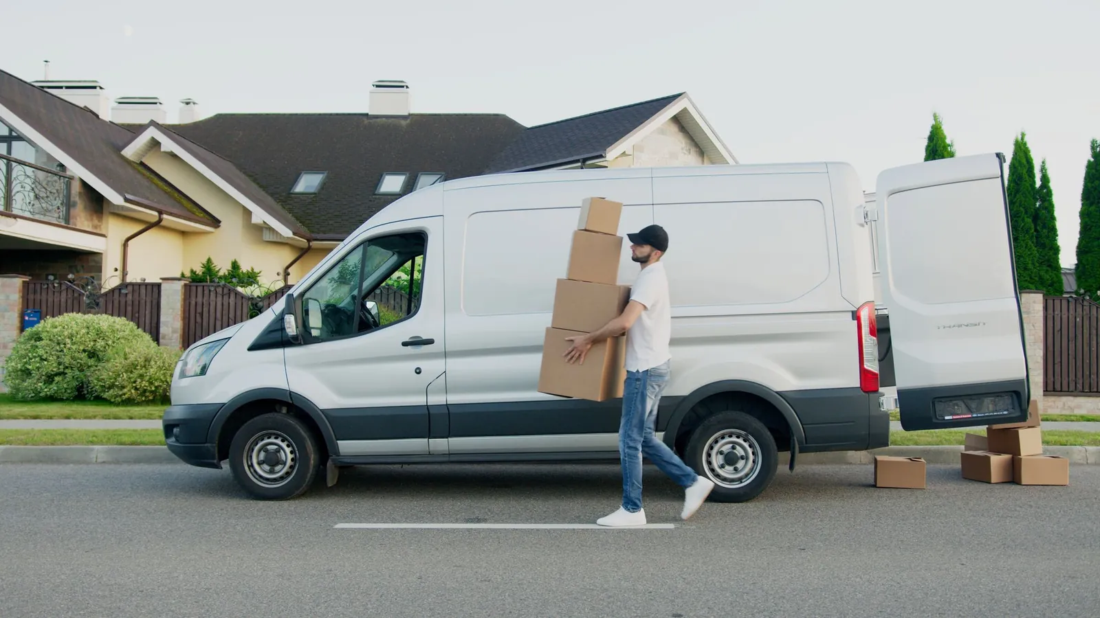Side view of a plain white Ford Transit-style cargo van parked on a suburban street, rear doors open