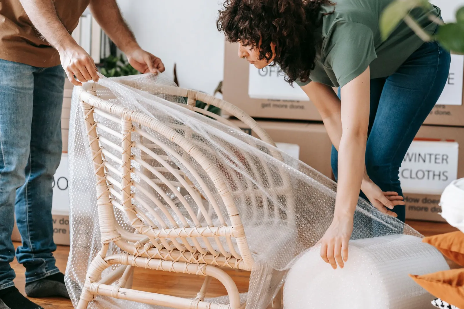 Couple wrapping a rattan armchair in bubble wrap from a large roll